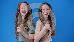 4k video of two twin girls showing thumbs up over blue.