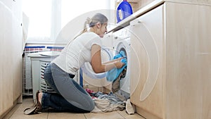 4k video of young housewife putting big pile of dirty clothes in washing machine