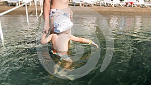 4k video of young mother holding her toddler son by hand and walking in sea water on beach