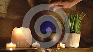 4k, Woman adding essential oil to electric diffuser lamp, candles on wooden table in room