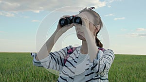 4K. A woman looks through binoculars. Standing in an endless green field