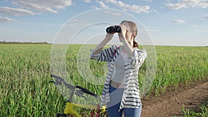 4K. A woman looks through binoculars. Standing in an endless green field