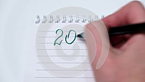 4K A woman`s hand writes the numbers of the year 2022 with a green felt-tip pen in a white notebook.