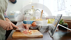 4K. woman slicing red tomato prepare ingredients for cooking follow cooking online video clip on website via tablet.