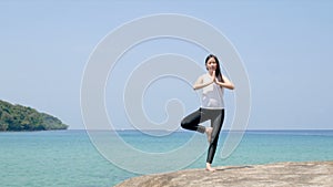 4K. a woman standing on one leg while practicing yoga on wooden bridge over the sea during summer vacation.