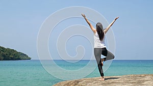 4K. a woman standing on one leg while practicing yoga on wooden bridge over the sea during summer vacation