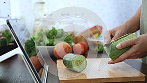 4K. Woman use finger slide on tablet screen and peel a cucumber, prepare ingredients for cooking follow cooking online video clip