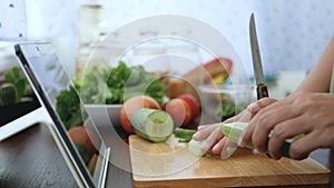 4K. woman use finger slide on tablet screen and peel a cucumber, prepare ingredients for cooking follow cooking online video clip