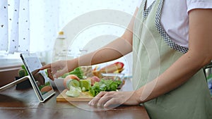 4K. Woman use finger slide on tablet screen and slicing fresh lettuce, prepare ingredients for cooking follow cooking online video