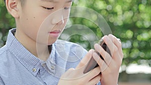 4k Young Asian boy play with smartphone in garden