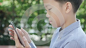 4k Young Asian boy play with tablet in a garden