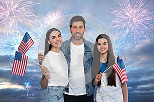 4th of July - Independence day of America. Happy family holding national flags of United States against sky with fireworks