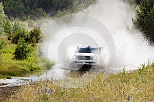 A 4wd car overcomes a water obstacle at high speed surrounded by spray