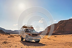 4WD off road vehicle parked in desert, backlight sun shines on mountains background - typical scenery of Wadi Rum, Jordan