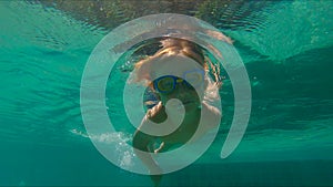 4x times slowmotion shot of a cute little boy diving into pool holding two pebbles under water in his hands