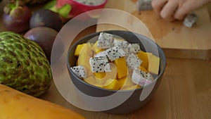 4x times Slowmotion shot of a young woman putting the dragon fruit cubes into a grey ceramic bowl and lots of tropical