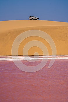 A 4x4 vehicle on a sand dune above a small salt lake.