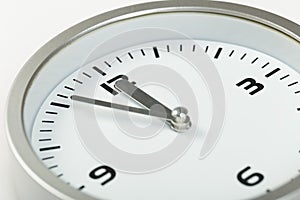 5 minutes to 12 white with light metal minimalistic clock close-up on a light background