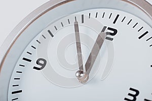 5 minutes to 12 white with light metal minimalistic clock close-up on a light background