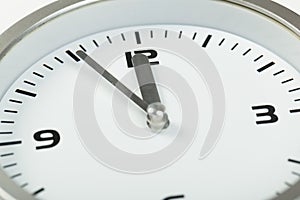 5 minutes to 12 white with light metal minimalistic clock close-up on a light background