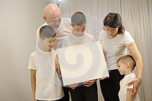 5 people three boys mom and dad Beautiful smiling family in white T-shirts hold in hands the big blank banner and Look
