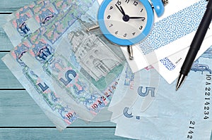 5 Ukrainian hryvnias bills and alarm clock with pen and envelopes. Tax season concept, payment deadline for credit or loan.