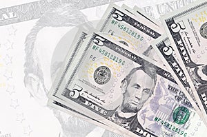 5 US dollars bills lies in stack on background of big semi-transparent banknote. Abstract presentation of national currency