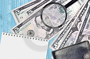 5 US dollars bills and magnifying glass with black purse and notepad. Concept of counterfeit money. Search for differences in