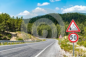 50 km h speed limit and warning signs on the winding asphalt road going through the forest on the mountain