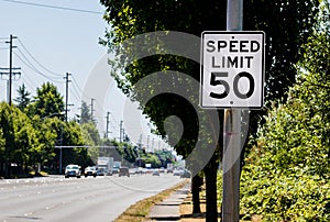 50 mph speed limit sign on post with a road and tree