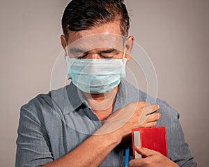 50`s man holding bible and praying god with medical face mask wearing to protect from covid-19 or coronavirus pandemic -