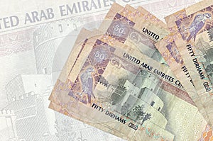 50 UAE dirhams bills lies in stack on background of big semi-transparent banknote. Abstract presentation of national currency