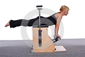 A 50-year-old trainer practices Pilates on an elevator chair, lying on her stomach supporting herself with her arms