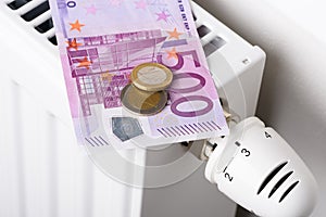 500 euro banknote with coins on heating radiator battery with thermostat temperature regulator