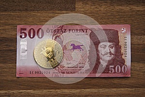 500 HUF banknote Portrait of II. Ferenc RÃ¡kÃ³czi. Brown wooden table. Next to it is a gold bitcoin digital cryptocurrency coin.