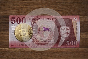 500 HUF banknote Portrait of II. Ferenc RÃ¡kÃ³czi. Brown wooden table. Next to it is a gold bitcoin digital cryptocurrency coin.