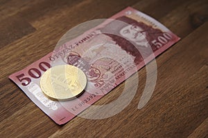 500 HUF banknote Portrait of II. Ferenc RÃ¡kÃ³czi. Brown wooden table. Next to it is a gold bitcoin digital cryptocurrency coin.