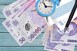 50000 Romanian leu bills and alarm clock with pen and envelopes. Tax season concept, payment deadline for credit or loan.