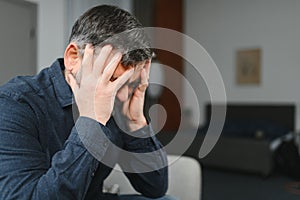 50s man hides his face with hands looking desperate close up, aged male sit on couch at home thinking search decision