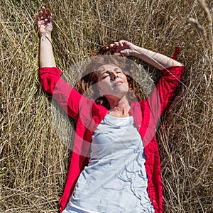 50s woman enjoying sun warmth sleeping alone on summer grass