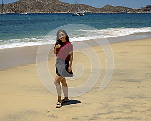 57 year-old Korean tourist standing on Medano Beach with the Sea of Cortez and moored boats in the background in Cabo San Lucas.