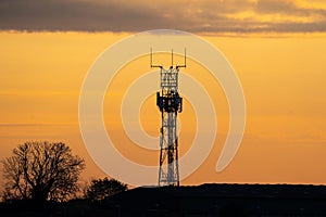 5G controversial radio mobile telephone broadcast transmitter mast silhouette at golden hour sunset. Summer sky with clouds