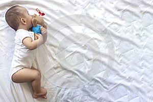 6-8-month-old baby boy lying playfully in bed. Charming 6-7 month little baby in white bodysuit. Baby boy in white bedding. Copy