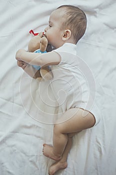 6-8-month-old baby boy lying playfully in bed. Charming 6-7 month little baby in white bodysuit. Baby boy in white bedding. Copy