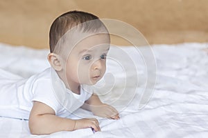 6-8-month-old baby boy lying playfully in bed. Charming 6-7 month little baby in white bodysuit. Baby boy in white bedding. Copy