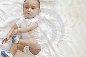 6-8-month-old baby boy lying playfully in bed. Charming 6-7 month little baby in white bodysuit. Baby boy in white bedding. Copy