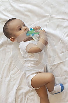 6-8-month-old baby boy lying playfully in bed. Charming 6-7 month little baby in white bodysuit. Baby boy in white bedding. Copy