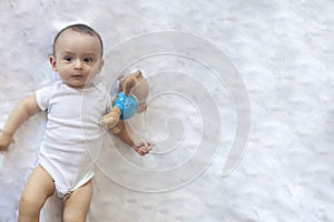 6-8-month-old baby boy lying playfully in bed. Charming 6-7 month little baby in white bodysuit. Baby boy in white bedding. Copy