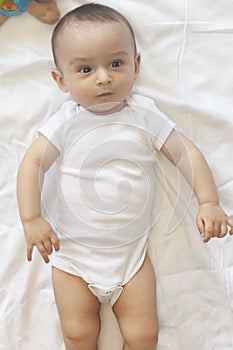 6-8-month-old baby boy lying playfully in bed. Charming 6-7 month little baby in white bodysuit. Baby boy in white bedding. Copy