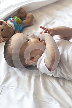 6-8-month-old baby boy lying playfully in bed. Charming 6-7 month little baby in white bodysuit. Baby boy in white bedding. Copy